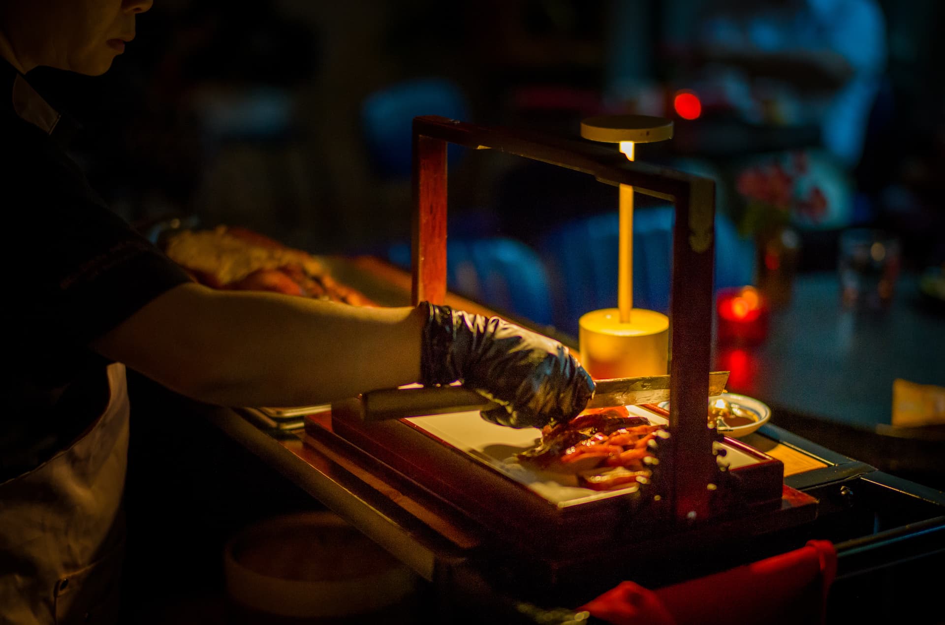 Chef carving Peking duck tableside under warm lamp light