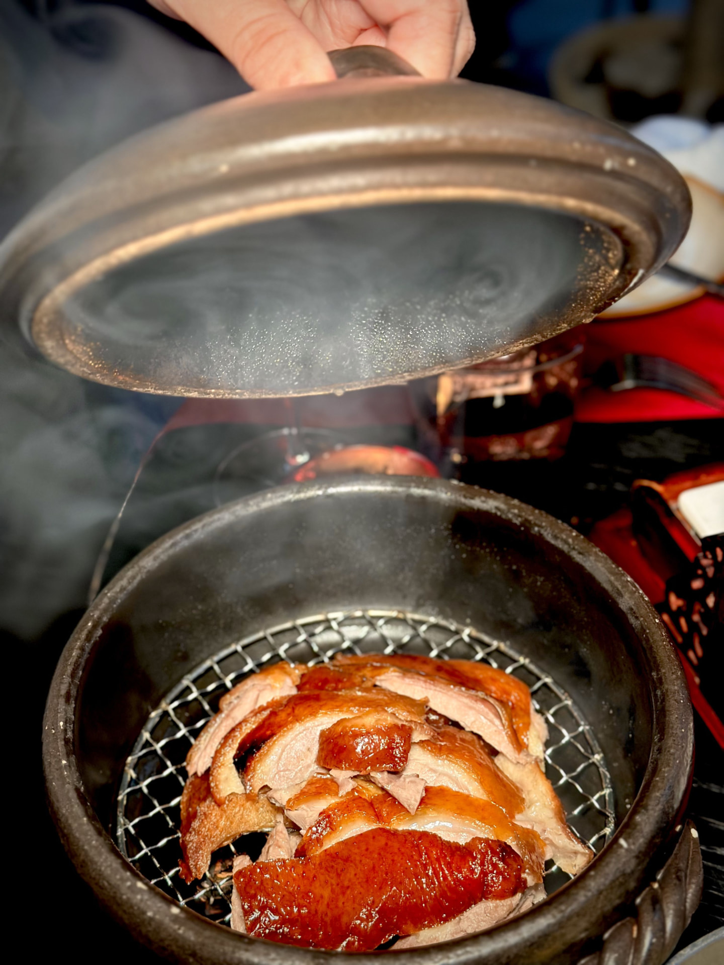 Lid lifted on a smoking clay pot of lychee-wood smoked duck